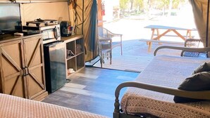 A tented accommodation with two beds, a kitchenette, and a view of the outdoors.