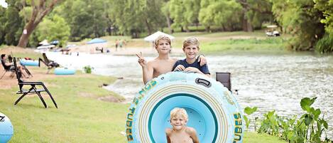 Two children sitting on a blue inflatable tube with a river in the background.
