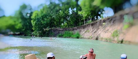 A group of people in a river setting, some in the water and others on the bank.