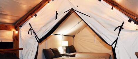 A tented room with a bed, a chair, and a table.