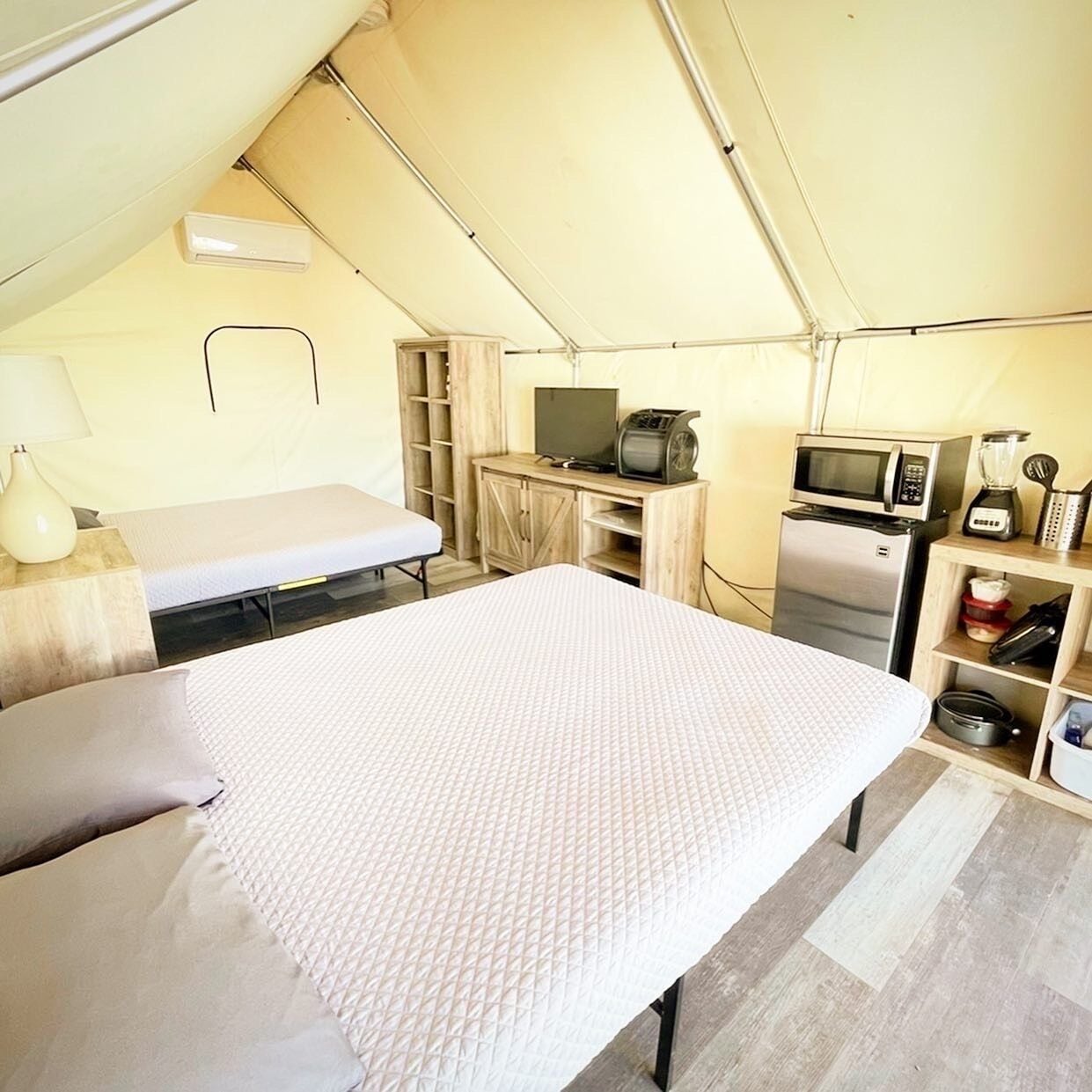 Een tentaccomodatie met een bed, een televisie, een magnetron en een koelkast.