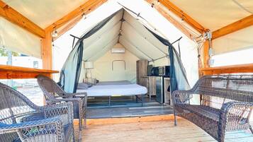 A tented accommodation with a bed, a table, and wicker chairs.