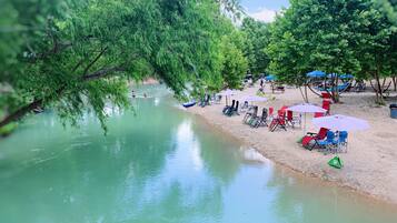 A riverside area with a sandy beach, several beach chairs, and umbrellas.