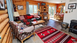 A log cabin interior with a sofa, armchair, wooden table, and a fireplace.