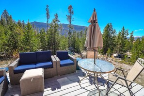 An outdoor deck with wicker furniture, a glass table, and an umbrella.