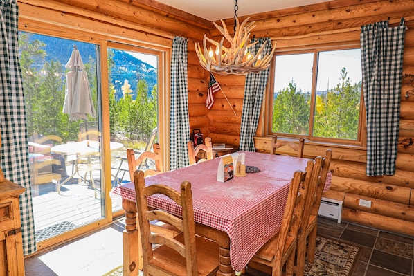 A wooden cabin with a dining area featuring a red and white checkered tablecloth, wooden chairs, and a chandelier made of antlers.