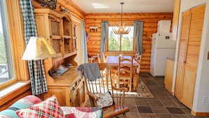 A cozy cabin interior with a dining area, wooden furniture, and a kitchen with a refrigerator.