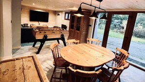 A cozy wooden dining area with a round table and chairs, a foosball table, and a TV mounted on the wall.