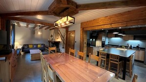 A rustic interior with a wooden dining table, chairs, a sofa, and a kitchen area.