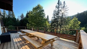 A wooden deck with picnic tables and a railing overlooking a forested area.