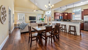 Una cocina amplia con suelo de madera, un comedor con una mesa grande y sillas, y una isla central con taburetes de bar.
