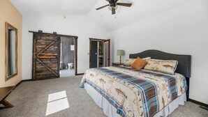 Une chambre avec un grand lit, un ventilateur de plafond et une porte coulissante de style rustique.