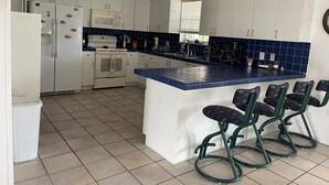 Cocina moderna con armarios blancos, encimera azul y una isla central con taburetes de bar.