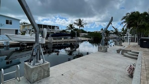 Un puerto deportivo con barcos amarrados, un paseo marítimo de hormigón y palmeras bajo un cielo nublado.