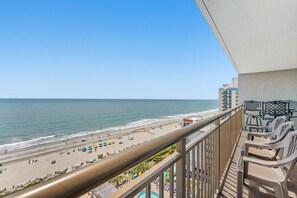Ein Balkon mit Blick auf einen Strand, Gartenmöbel und ein Gebäude im Hintergrund.