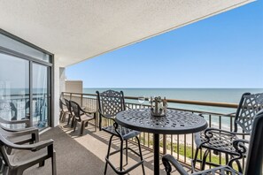 Ein Balkon mit Tisch und Stühlen mit Blick auf einen Strand.