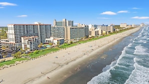 A beachfront hotel with multiple high-rise buildings, a sandy beach, and ocean waves.