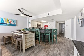 A modern kitchen with a dining area, a ceiling fan, and a painting on the wall.
