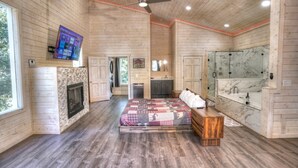 Ein geräumiges Schlafzimmer mit einem großen Bett, Holzboden, Kamin, Fernseher und einem Badezimmer mit Marmorwaschtisch.