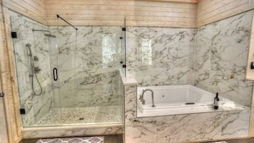 A bathroom with a glass-enclosed shower, a marble-tiled wall, and a freestanding bathtub.