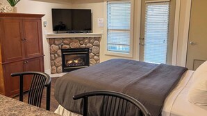 Un dormitorio con cama, chimenea, televisor y pared de piedra.