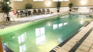 Una piscina interior con agua cristalina, solárium con baldosas, sillones de descanso y plantas en macetas.