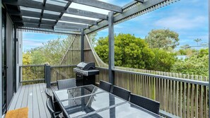 A covered outdoor area with a grill, glass-top table, and wicker chairs. - Harmony on Nautilus Inverloch (Inverloch)