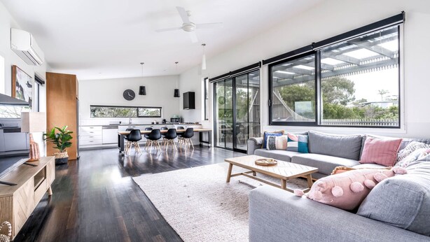 A modern living room with a grey sofa, a wooden coffee table, and a dining area with a black table and chairs. - Harmony on Nautilus Inverloch (Inverloch)