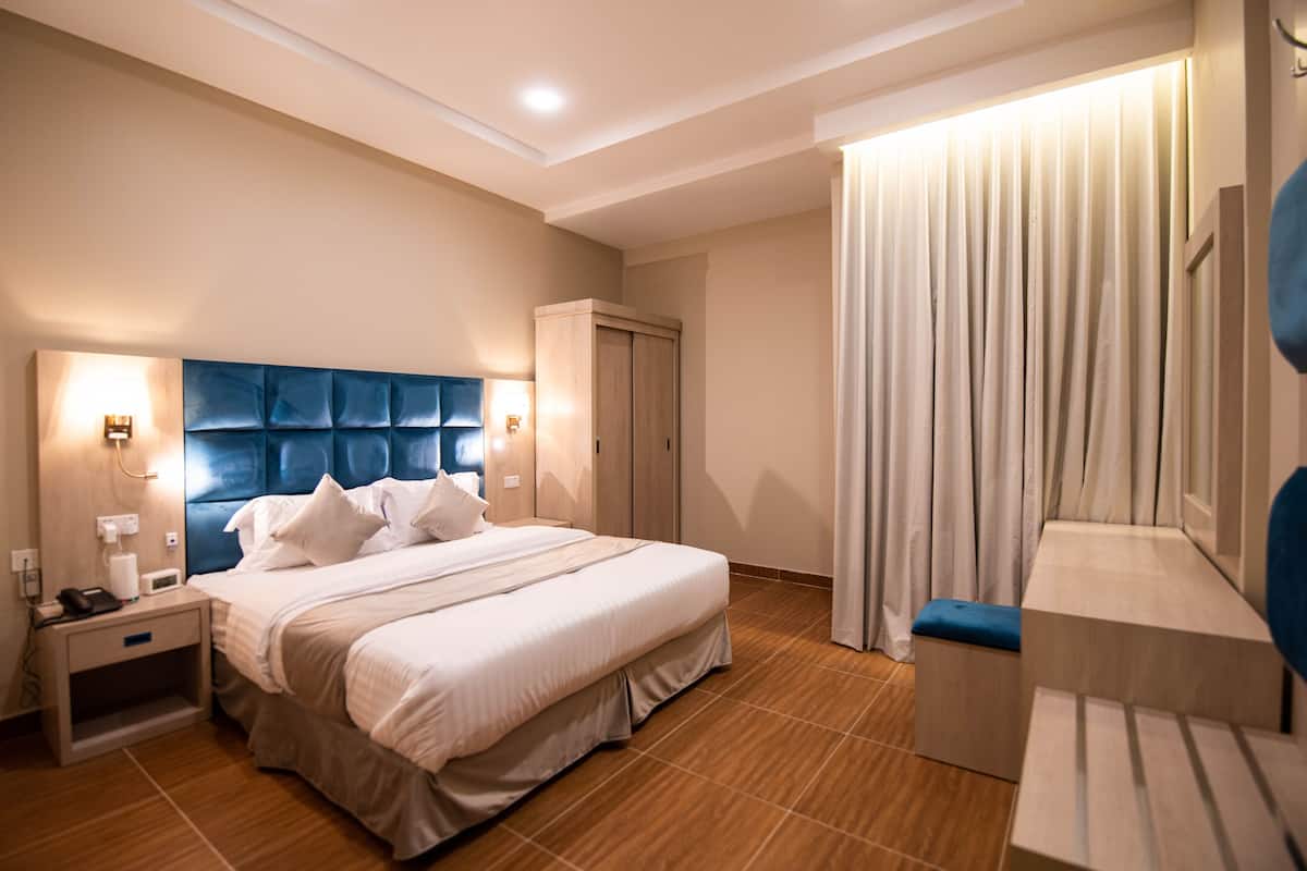 Una camera d'albergo moderna con un letto grande, un comodino, un armadio e un'area salotto con una panca e un tavolo.