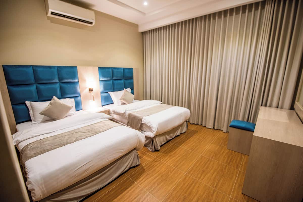 Camera d'albergo con due letti, pavimento in legno, un'ampia finestra con tende e una piccola area salotto.