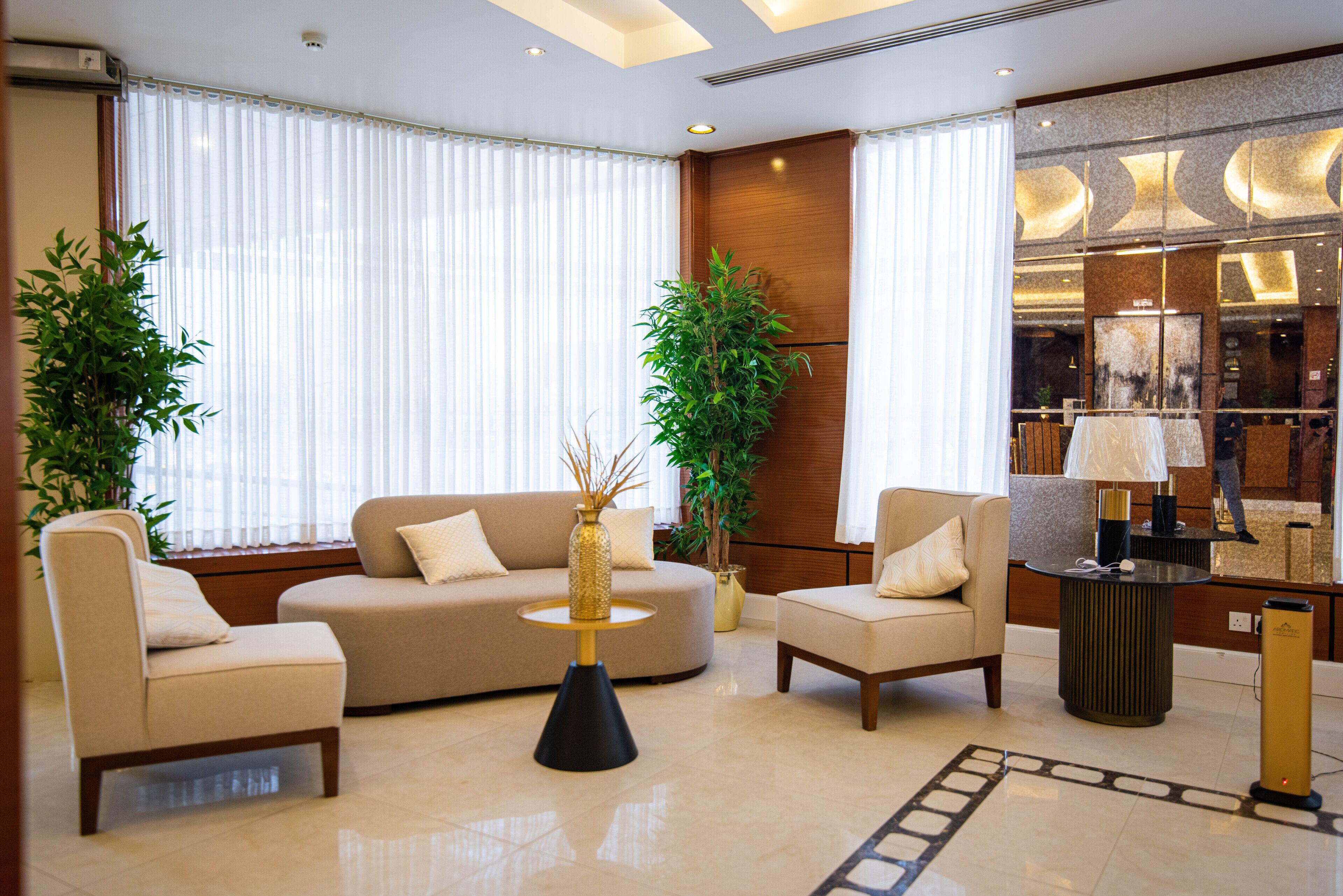 Un moderno vestíbulo de hotel con un sofá color crema, dos sillones, una mesa de centro redonda y una planta grande en maceta.
