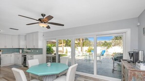 Een moderne keuken met witte kasten, een eethoek met een turquoise tafel en witte stoelen, en een grote schuifdeur die leidt naar een terras.