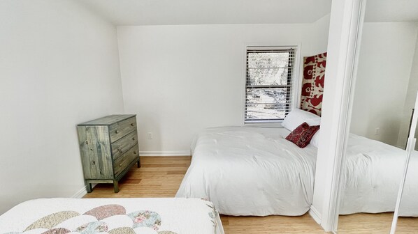 A bedroom with a bed, a dresser, and a window with blinds. - Lake Travis Bungalow in Jonestown (Jonestown)