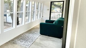 Et rummeligt værelse med store vinduer, en grøn sofa og et mønstret tæppe.