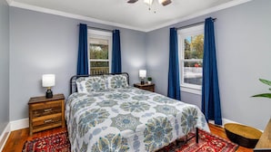 A bedroom with a bed, two bedside tables, a ceiling fan, and two windows with curtains.