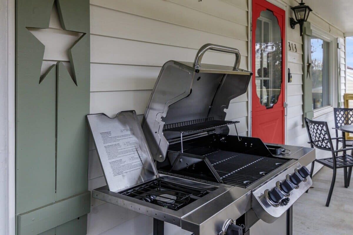 Een buitenbarbecue met een gasbrander en een bijbehorende brander, geplaatst voor een huis met een rode deur en een sterdecoratie op de muur.