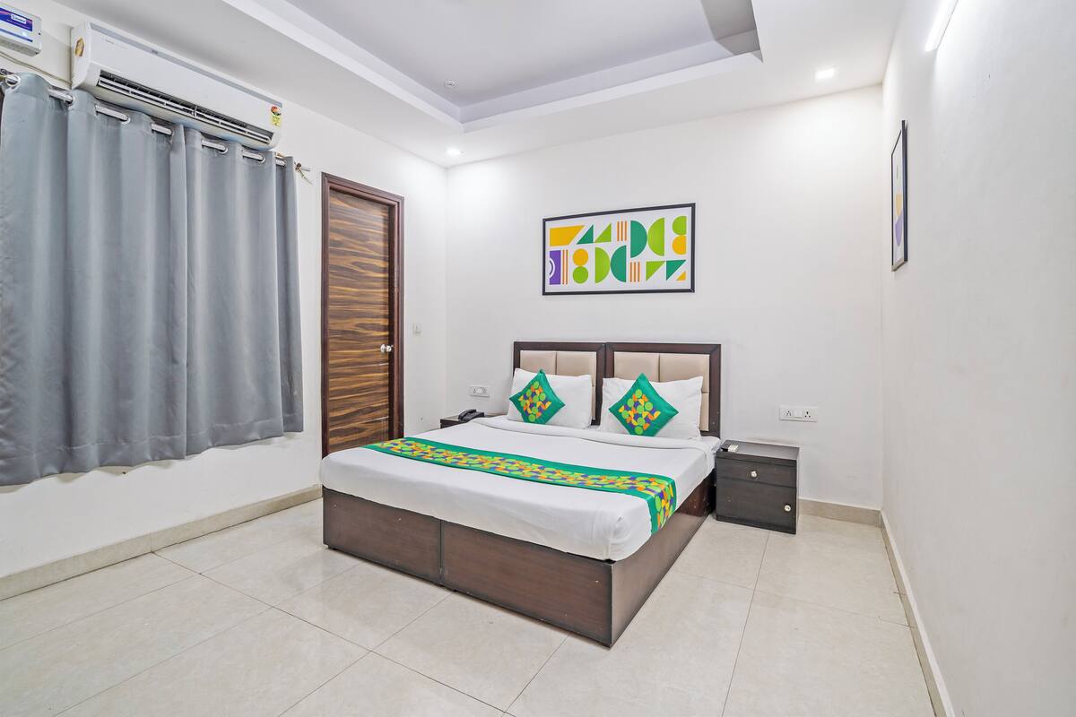 A bedroom with a bed, a bedside table, a wall-mounted air conditioner, and a door.