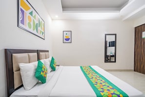 A hotel room with a bed, pillows, a mirror, and artwork on the walls. - Treebo Modern Stays (Noida)