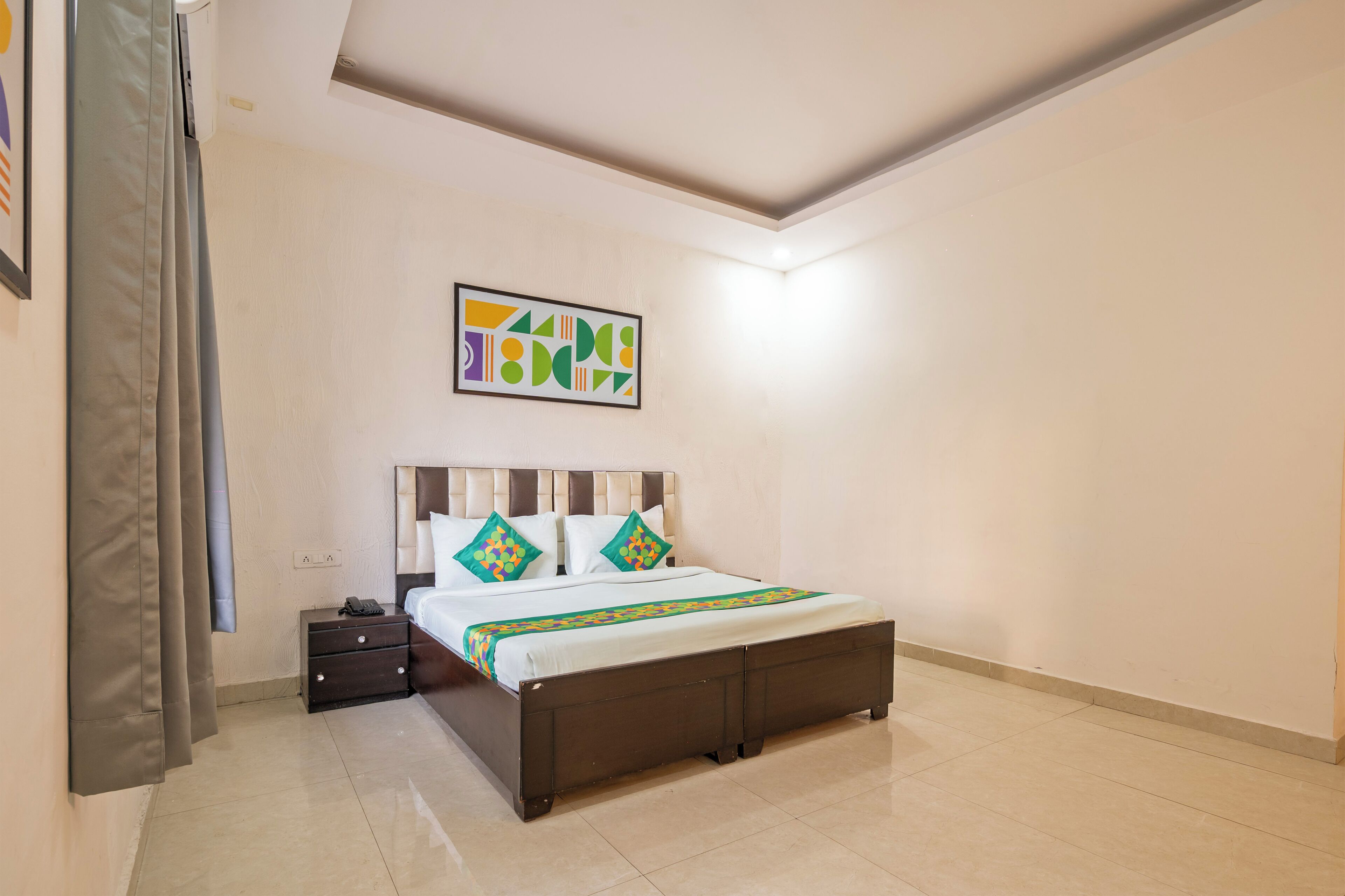 A neatly made bed with a headboard, a bedside table with a phone, and a wall-mounted artwork.