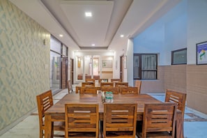 A spacious dining area with a large wooden table and chairs, a patterned wall, and a view of the outdoors. - Treebo Modern Stays (Noida)