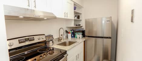 Una cocina compacta con estufa de acero inoxidable, refrigerador y armarios blancos.