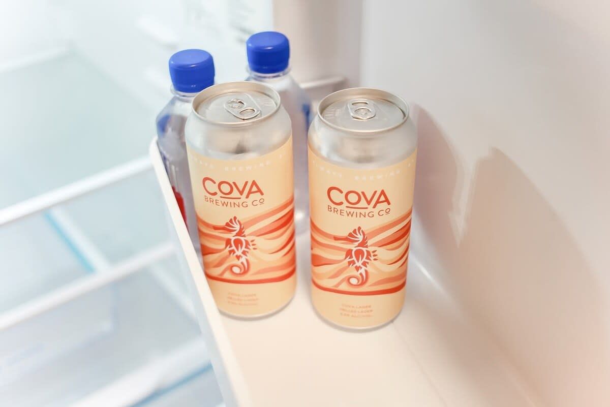 Two cans of Cova Brewing Co. on a white shelf.