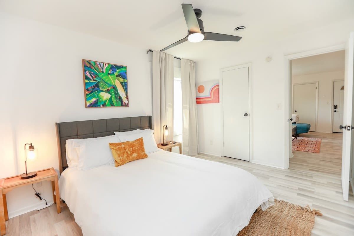 Une chambre à coucher avec un lit, un ventilateur de plafond, une table de chevet, une lampe et un tableau au mur.