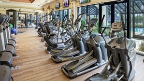 Een sportschool met meerdere loopbanden in rijen, grote ramen en uitzicht op een zwembad.