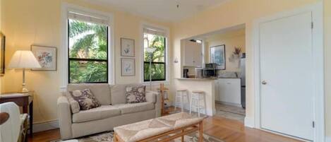 A living room with a sofa, a bench, a lamp, and a window with a view of greenery.