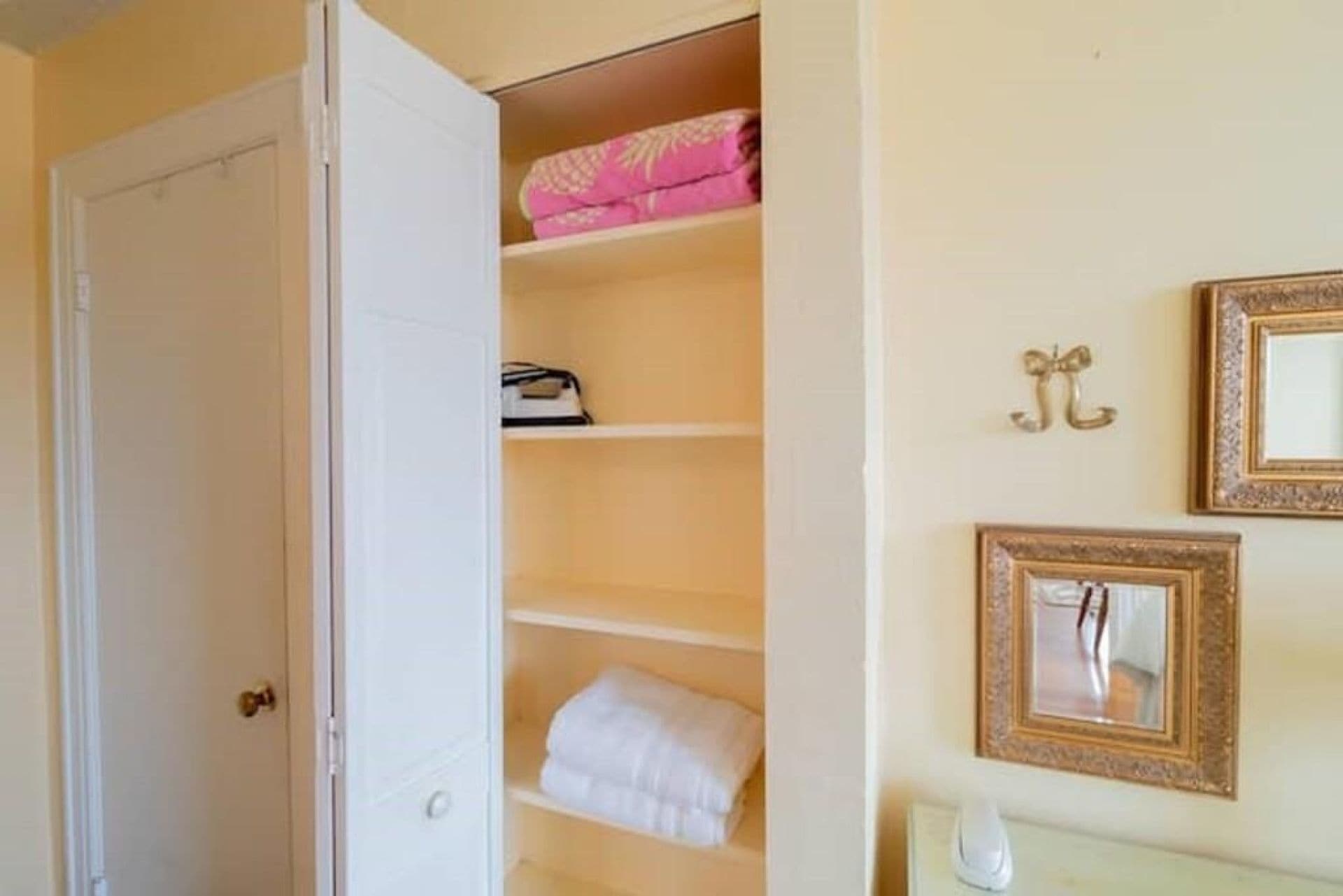 A room with a white door, a closet with shelves, and two framed mirrors on the wall.