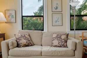 A beige sofa with floral cushions, a lamp, and framed botanical prints on the wall.