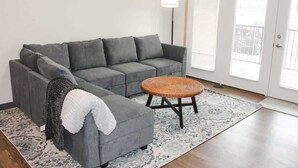 A grey sofa, a small round stool, a patterned rug, a floor lamp, and a door with blinds. - 2 Bedroom Apartment Downtown Sun Prairie! (Sun Prairie)