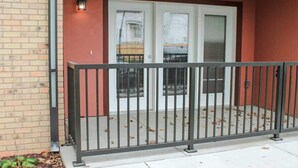 A building entrance with a number '205' above the door, a metal railing in front, and a brick wall to the left. - 2 Bedroom Apartment Downtown Sun Prairie! (Sun Prairie)