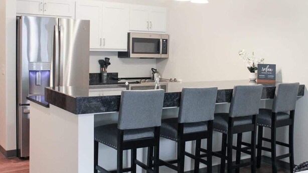 A modern kitchen with a refrigerator, microwave, and bar stools. - 2 Bedroom Apartment Downtown Sun Prairie! (Sun Prairie)